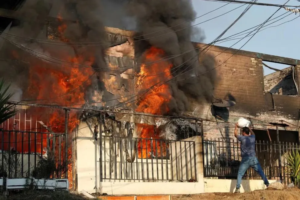 Un hombre intenta extinguir el fuego de una casa.